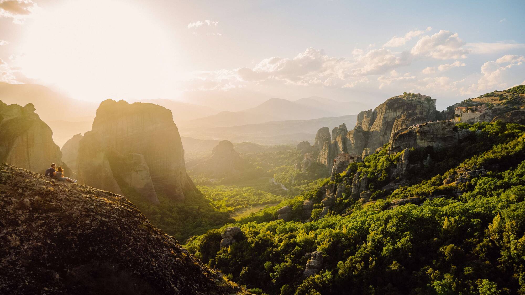 Couple sitting on top of a mountain overlooking a valley