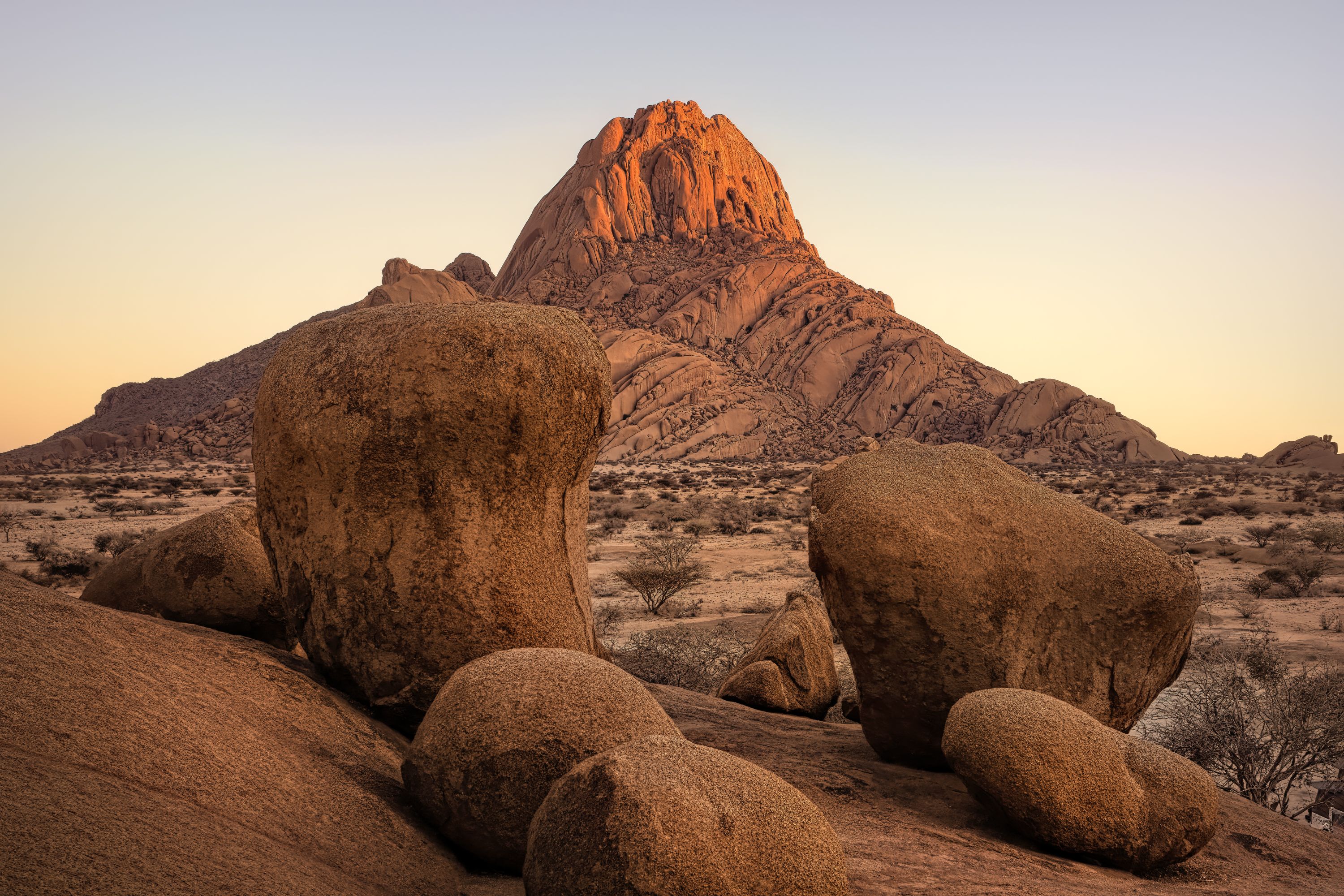Large rocks in the foreground and a tall rocky mountain in the background in the Red Dunes of Sossusvei in Namibia.
