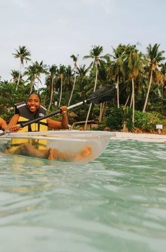 Two young travellers kayaking in a transparent kayak in crystal clear waters off a palm-lined beach in Palawan Philippines - Philippines Island Hopping West Tour