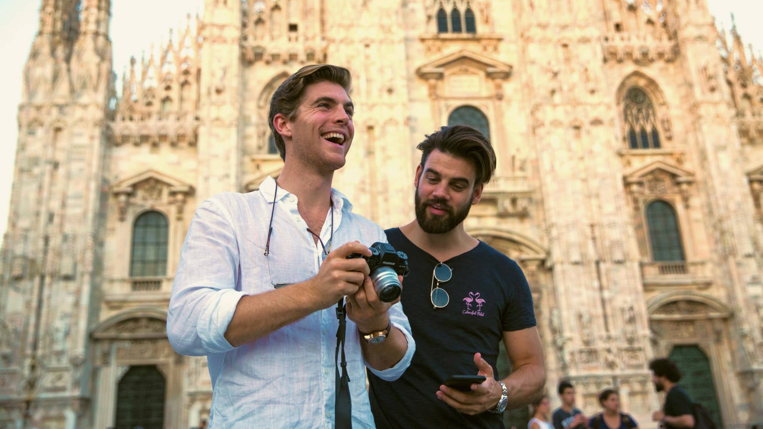 Two Contiki travellers reviewing photos in front of Milan Cathedral (Duomo di Milano), capturing memories while exploring Milan on the Tuscany, Milan & Venice 35 to 45 Tour