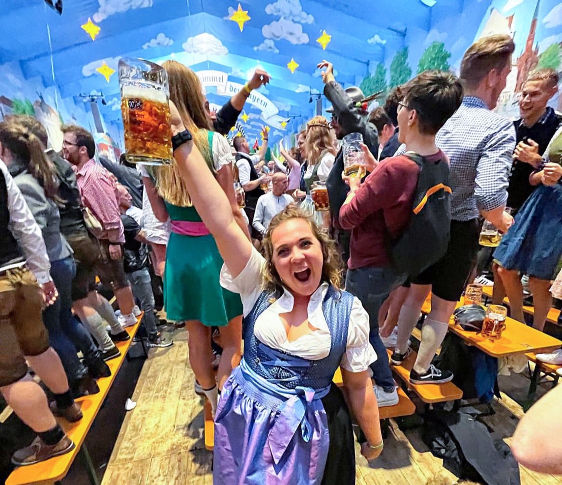 Traveller dressed wearing a dirndl, holding a stein, and standing in an Oktoberfest tent in Munich, Germany
