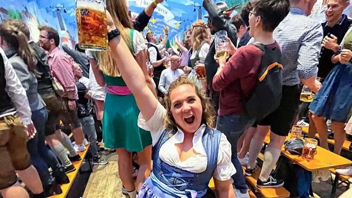 Traveller dressed wearing a dirndl, holding a stein, and standing in an Oktoberfest tent in Munich, Germany