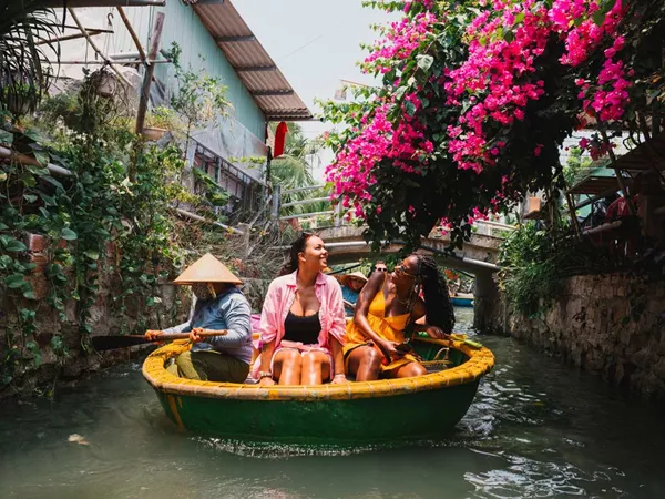 People Enjoying A Basket Shape Boat Ride In A Narrow River Flowers Around