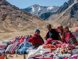 Three friends and a local person smiling traditional fabrics in Peru.