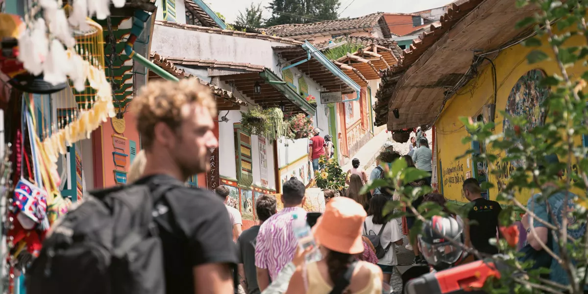 Travellers exploring the vibrant colourful colonial streets of Guatapé in Antioquia Colombia lined with painted buildings and artisan market stalls - Contiki Best of Colombia Tour