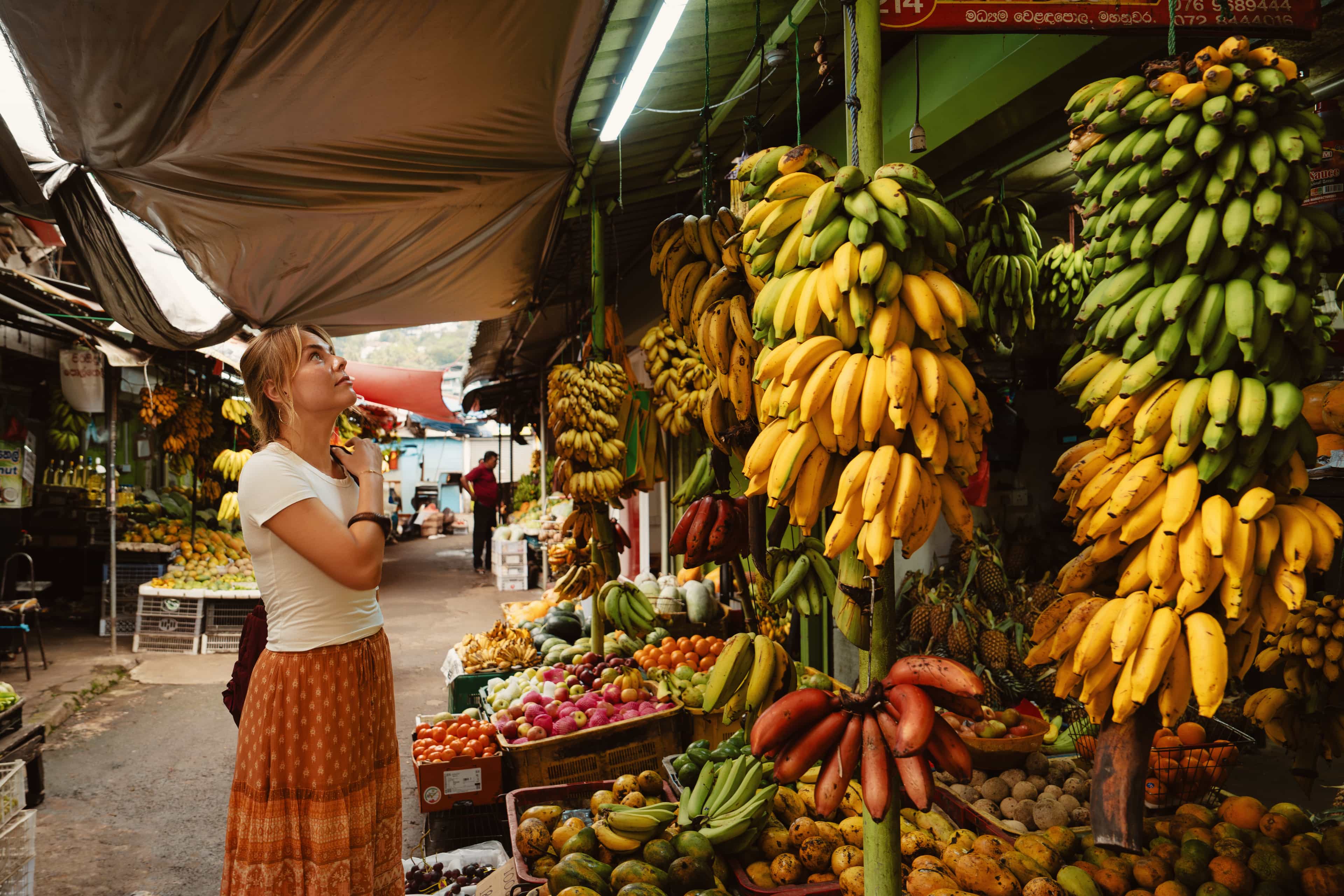 Traveller browsing towering bunches of bananas and fresh produce at a local market in Sri Lanka.
