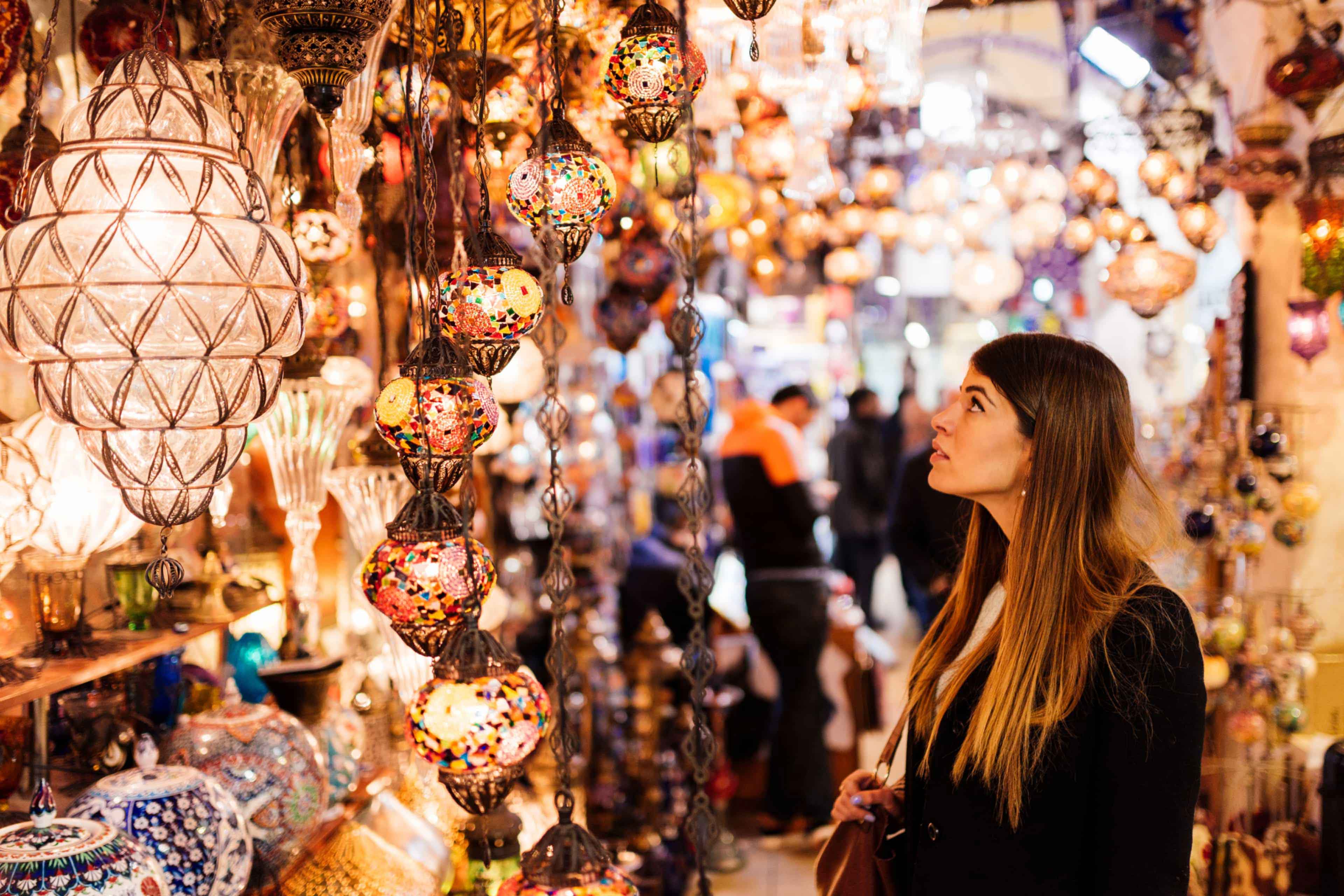 Traveller admiring colourful mosaic lamps hanging in the Grand Bazaar, Istanbul, Turkey.