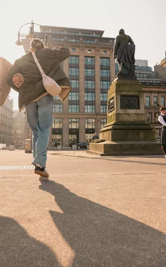 Travellers explore George Square in Glasgow while a bagpiper performs on the Contiki Best of England & Scotland Tour