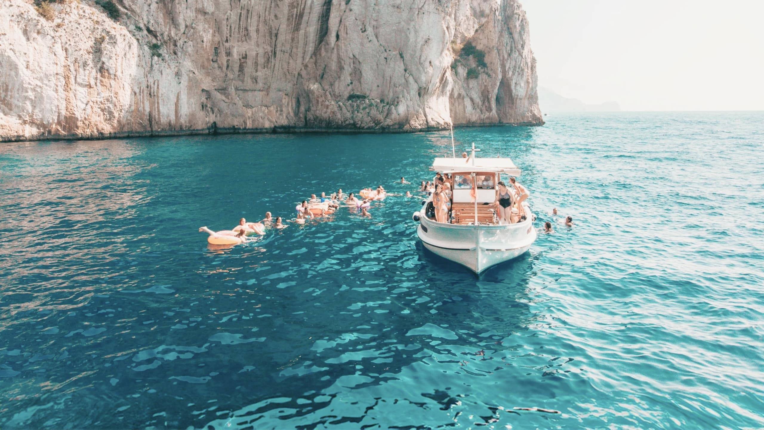Travellers swim from a boat in the turquoise waters off the coast of Capri on the Contiki Best of Italy Tour
