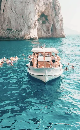 Travellers swim from a boat in the turquoise waters off the coast of Capri on the Contiki Best of Italy Tour