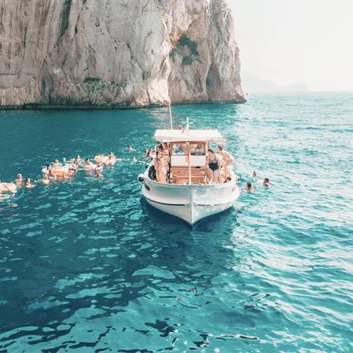 Travellers swim from a boat in the turquoise waters off the coast of Capri on the Contiki Best of Italy Tour