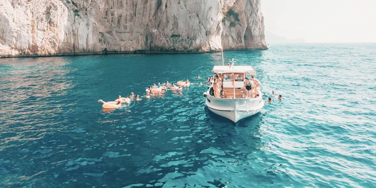 Travellers swim from a boat in the turquoise waters off the coast of Capri on the Contiki Best of Italy Tour