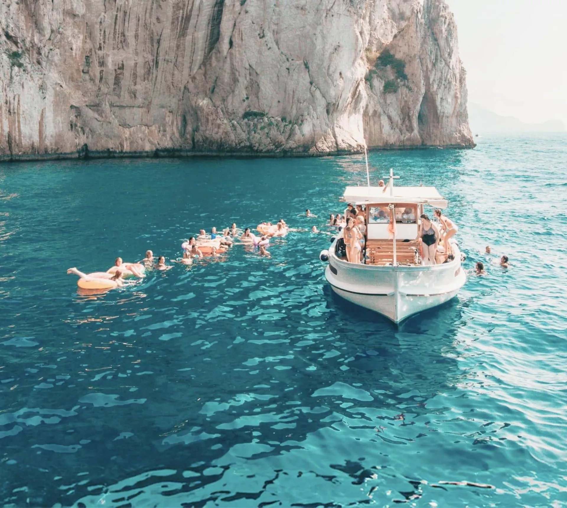 Travellers swim from a boat in the turquoise waters off the coast of Capri on the Contiki Best of Italy Tour