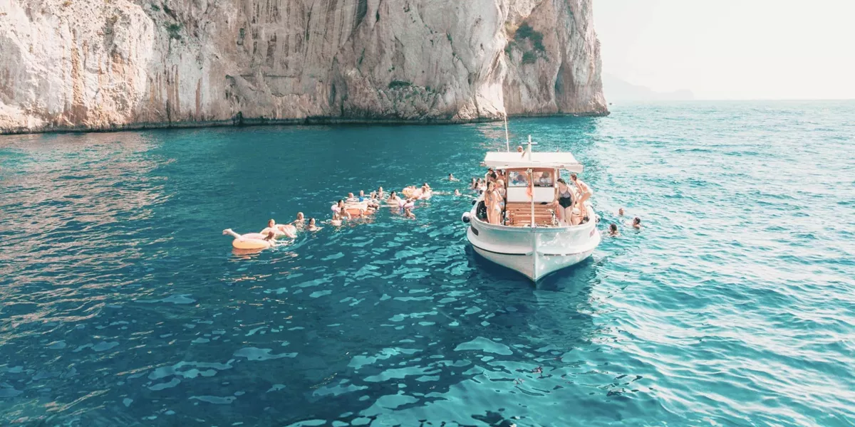Travellers swim from a boat in the turquoise waters off the coast of Capri on the Contiki Best of Italy Tour
