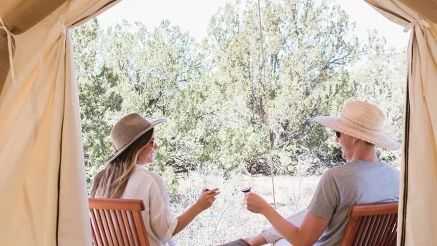 Couple in hats drinking wine near glamping tent
