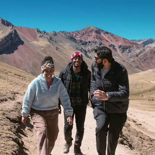 Contiki travellers hiking through the colourful Andes Mountains near Rainbow Mountain, Peru, surrounded by dramatic alpine scenery on the Ultimate South America Tour