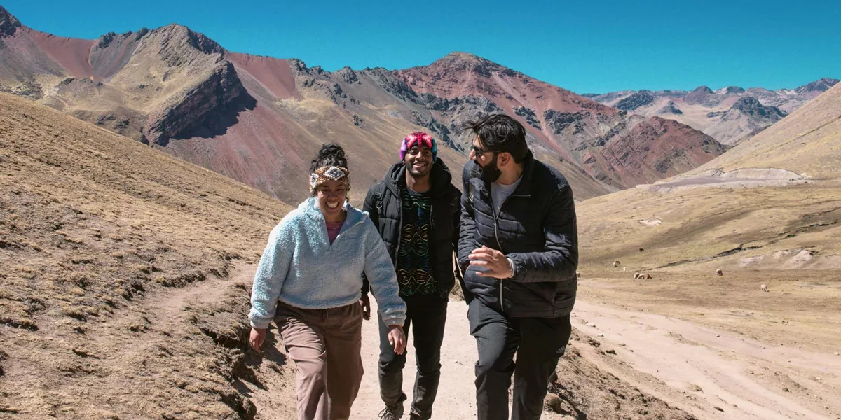 Contiki travellers hiking through the colourful Andes Mountains near Rainbow Mountain, Peru, surrounded by dramatic alpine scenery on the Ultimate South America Tour