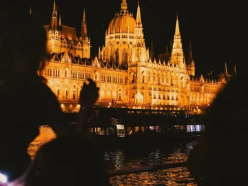 Travellers take in the glowing Hungarian Parliament Building from the Danube River during a night-time sightseeing experience in Budapest - Contiki Berlin to Budapest by Train Tour