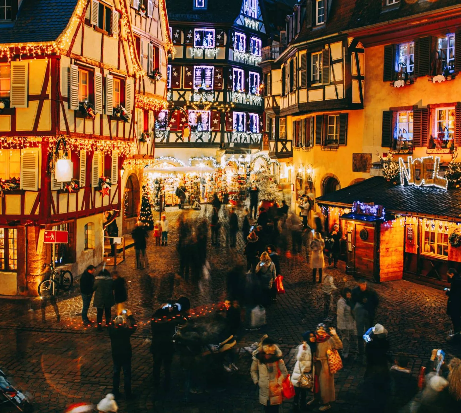 Aerial view of the festive Christmas market in France at night with illuminated half-timbered buildings and crowds of shoppers - Contiki French Christmas Markets Tour