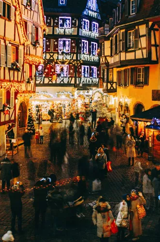 Aerial view of the festive Christmas market in France at night with illuminated half-timbered buildings and crowds of shoppers - Contiki French Christmas Markets Tour