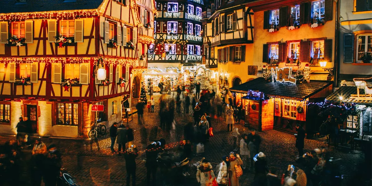 Aerial view of the festive Christmas market in France at night with illuminated half-timbered buildings and crowds of shoppers - Contiki French Christmas Markets Tour