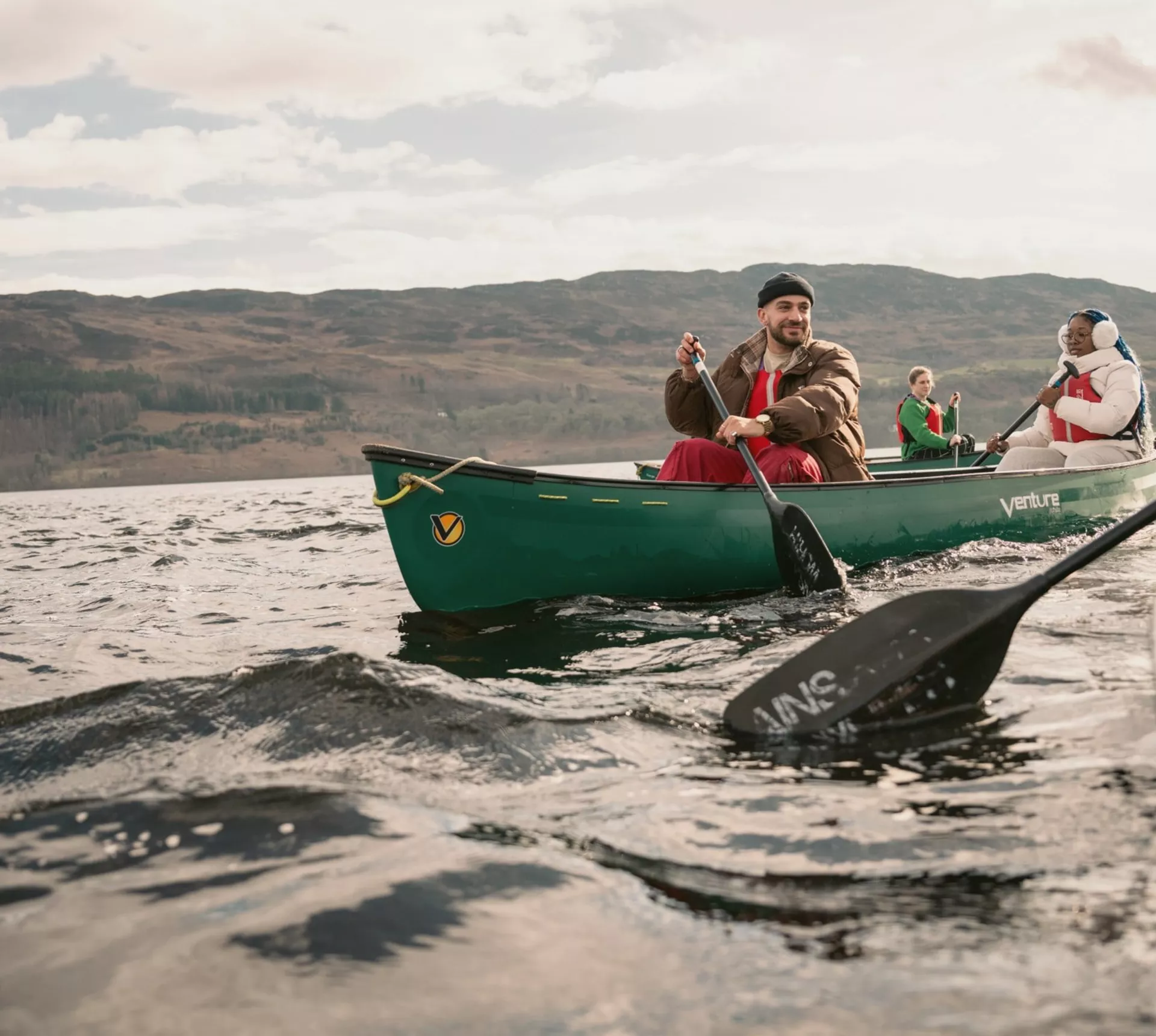 Contiki Travellers explore the Scottish Highlands by canoe, paddling across a tranquil loch with rolling hills in the background - Best of England & Scotland Summer Tour