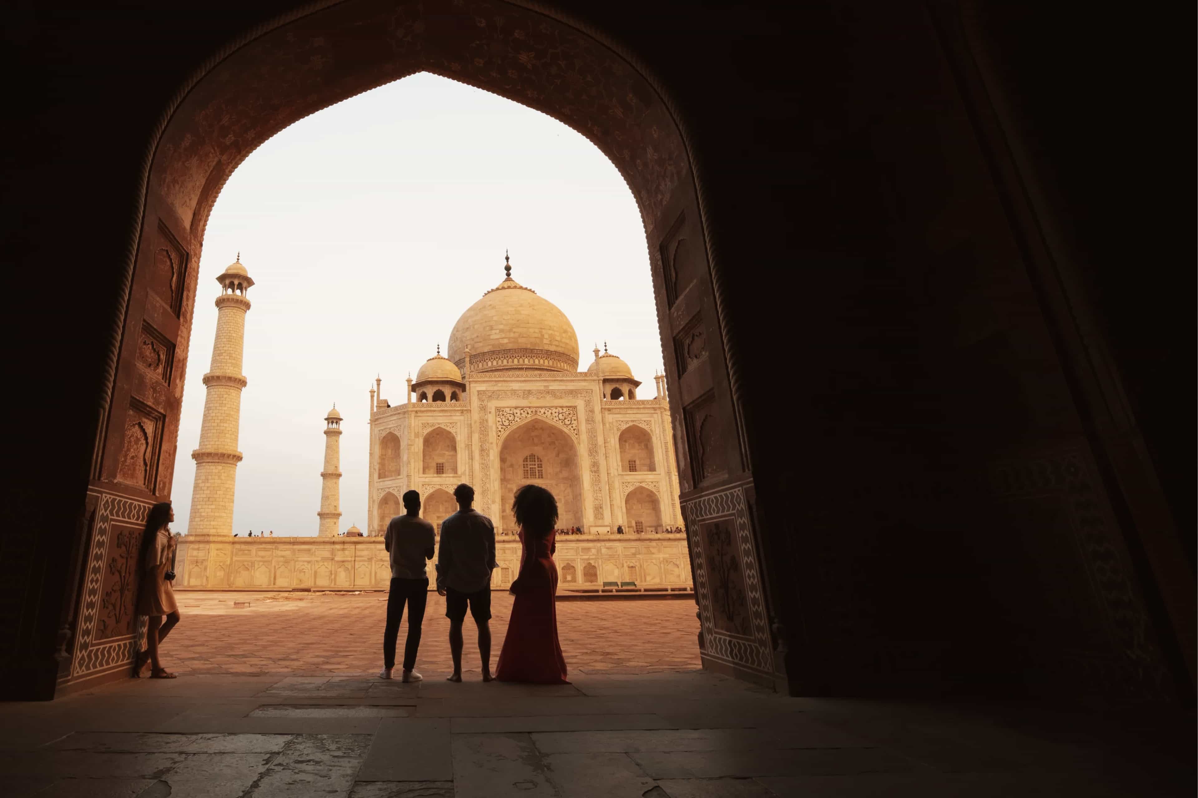 Travellers silhouetted in an archway framing the Taj Mahal, Agra, India.