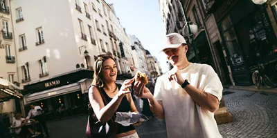 Travellers enjoying a French pastry while exploring a charming street on the Contiki France in a Week Tour