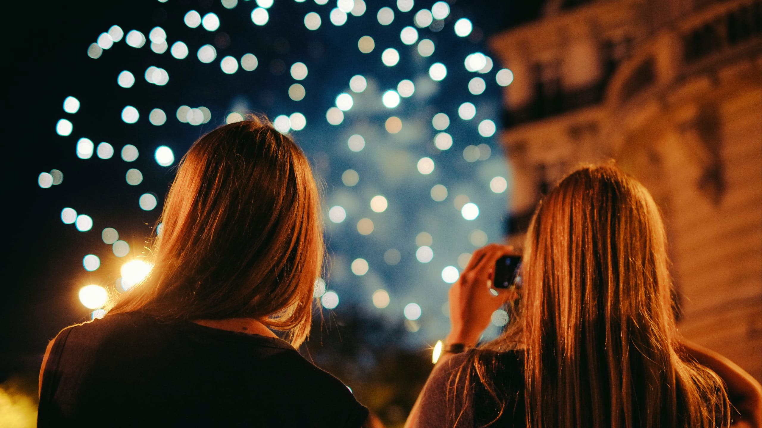 Two young women photographing New Year's Eve fireworks display in Paris France at night - Contiki Paris New Year's Eve Tour