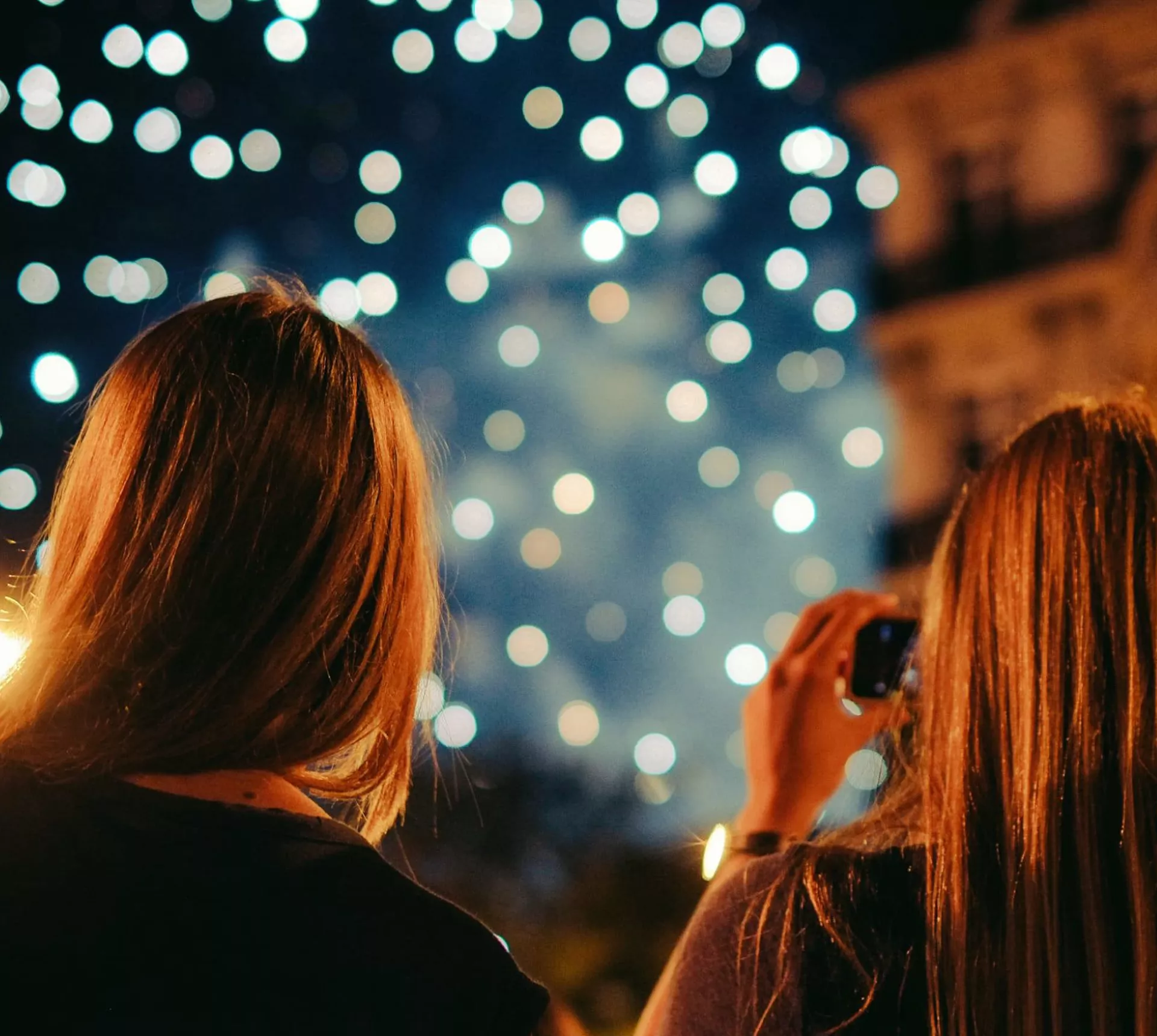 Two young women photographing New Year's Eve fireworks display in Paris France at night - Contiki Paris New Year's Eve Tour