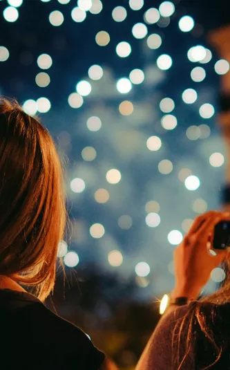 Two young women photographing New Year's Eve fireworks display in Paris France at night - Contiki Paris New Year's Eve Tour
