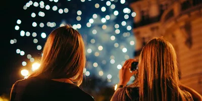 Two young women photographing New Year's Eve fireworks display in Paris France at night - Contiki Paris New Year's Eve Tour