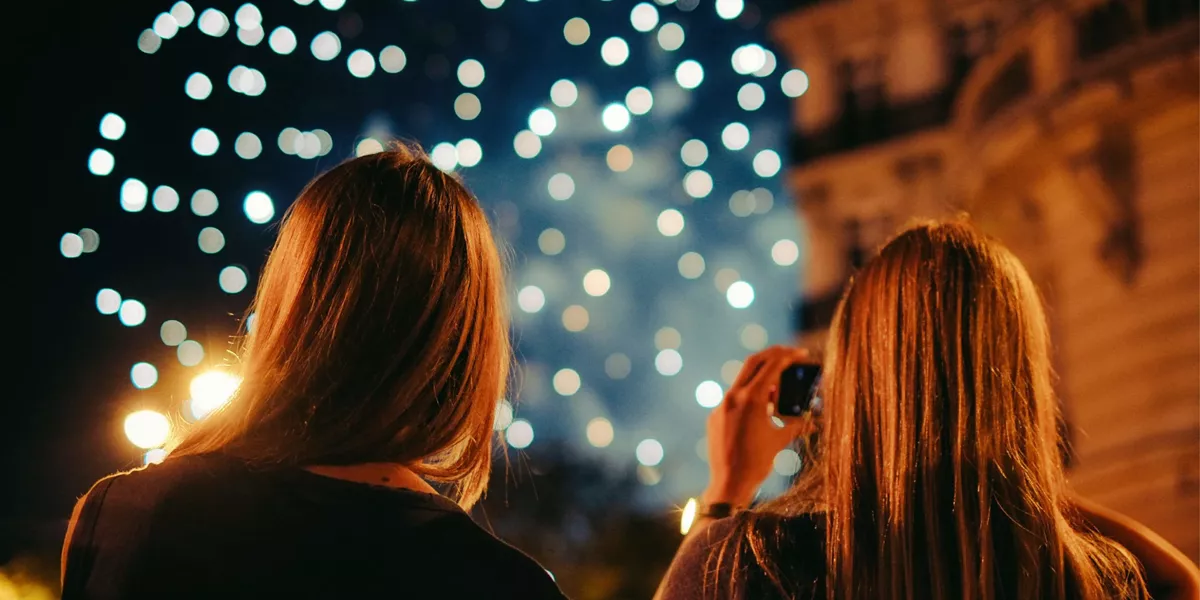 Two young women photographing New Year's Eve fireworks display in Paris France at night - Contiki Paris New Year's Eve Tour