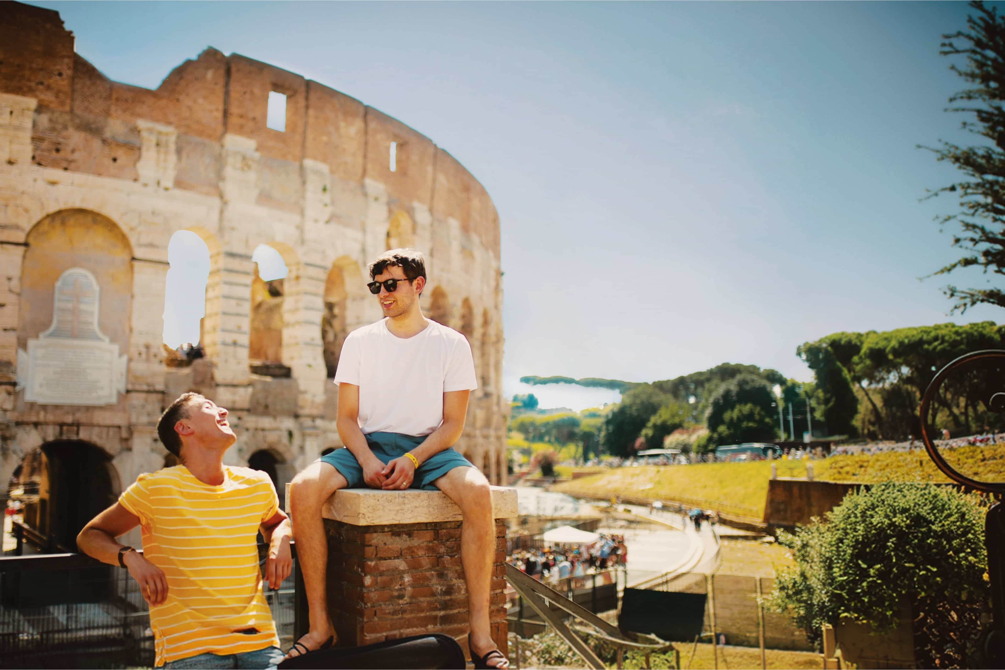 Two travellers laughing together in front of the Colosseum in Rome, Italy.