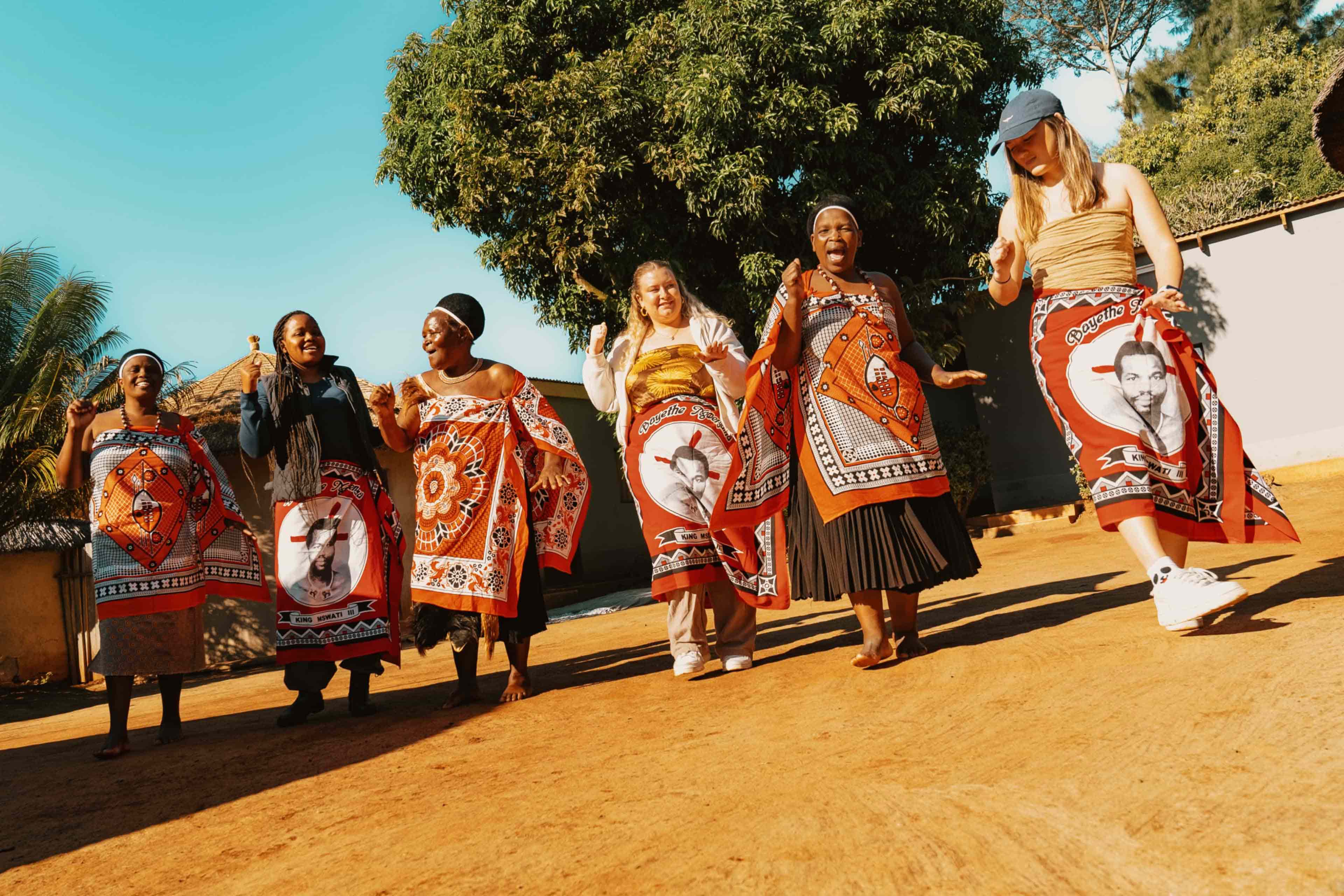 Travellers join local women in a traditional dance, wearing vibrant printed fabric on a South Africa trip.