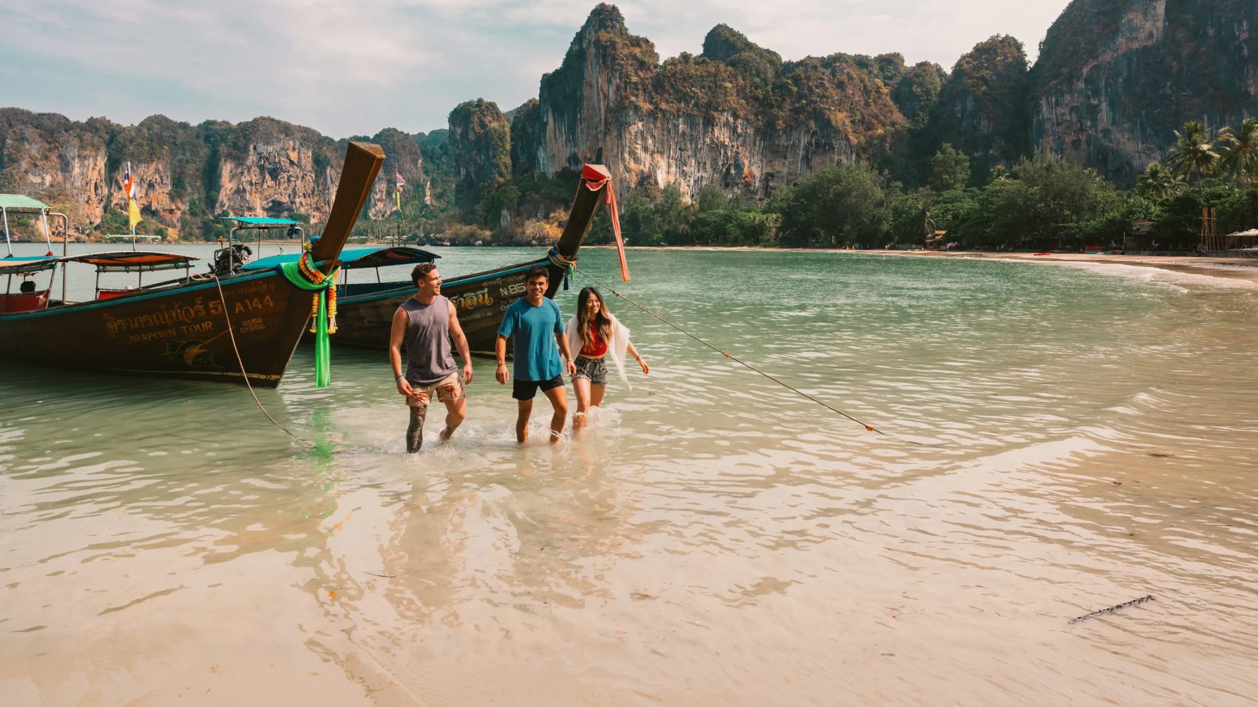 A group wading ashore from a traditional long-tail boat on a beach in Krabi - Contiki Southern Thailand: Khao Sok & Krabi Tour