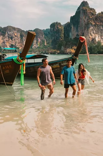 A group wading ashore from a traditional long-tail boat on a beach in Krabi - Contiki Southern Thailand: Khao Sok & Krabi Tour