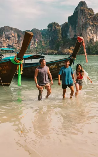 A group wading ashore from a traditional long-tail boat on a beach in Krabi - Contiki Southern Thailand: Khao Sok & Krabi Tour