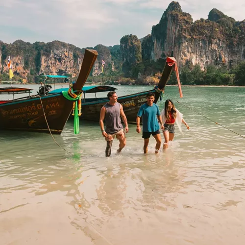 A group wading ashore from a traditional long-tail boat on a beach in Krabi - Contiki Southern Thailand: Khao Sok & Krabi Tour