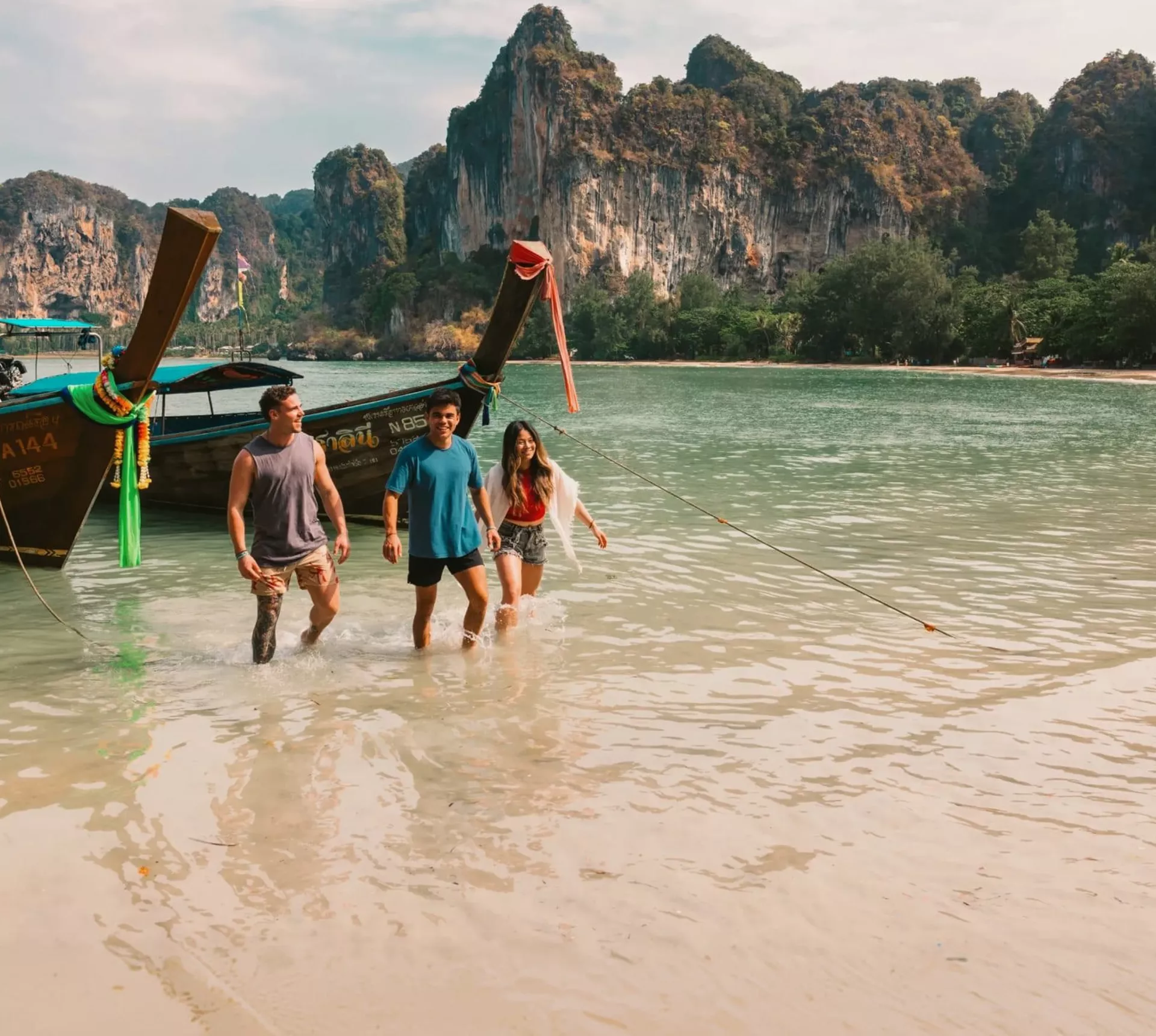 A group wading ashore from a traditional long-tail boat on a beach in Krabi - Contiki Southern Thailand: Khao Sok & Krabi Tour