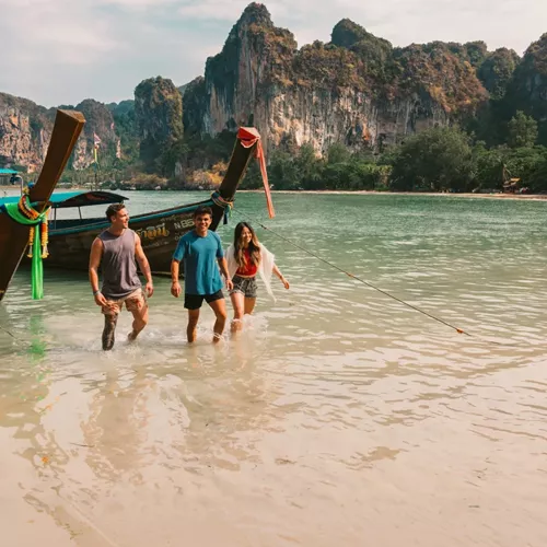 A group wading ashore from a traditional long-tail boat on a beach in Krabi - Contiki Southern Thailand: Khao Sok & Krabi Tour