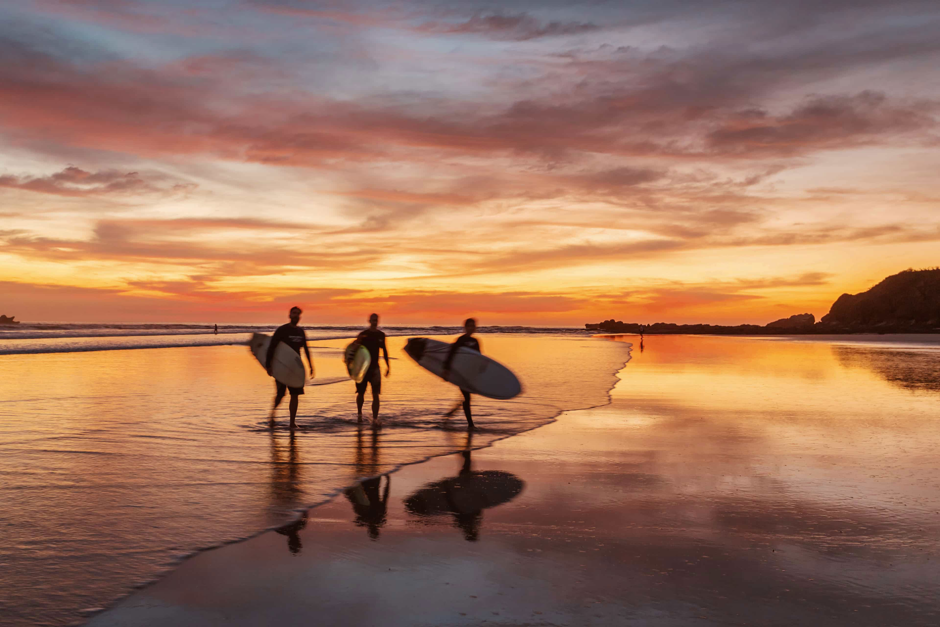 surfers-silhouetted-against-a-fiery-sunset-sky-carrying-boards-along-the-beach-in-costa-rica.jpg