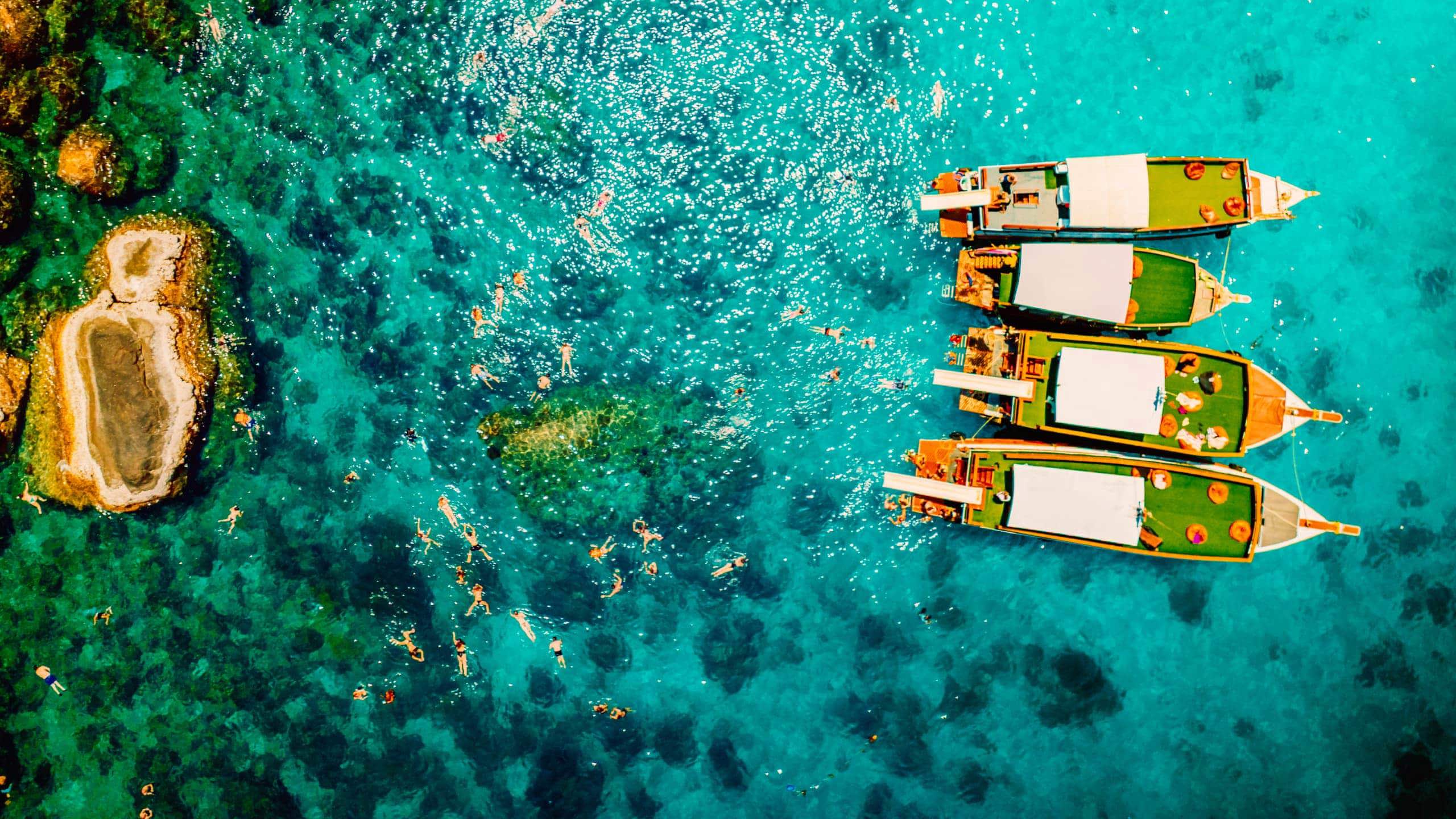 Contiki travellers swimming and snorkelling in vivid turquoise waters around traditional wooden boats anchored off the coast of a Thai island on a Thai Island Hopping East Tour