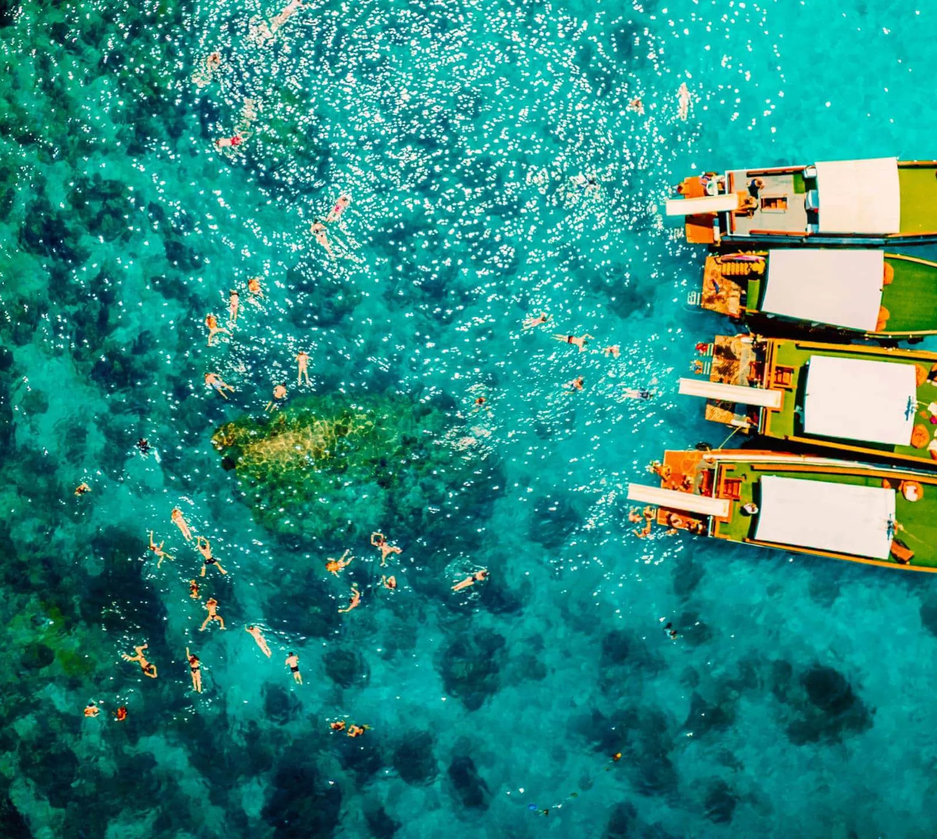 Contiki travellers swimming and snorkelling in vivid turquoise waters around traditional wooden boats anchored off the coast of a Thai island on a Thai Island Hopping East Tour