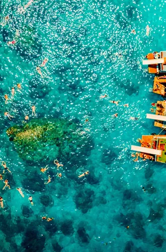 Contiki travellers swimming and snorkelling in vivid turquoise waters around traditional wooden boats anchored off the coast of a Thai island on a Thai Island Hopping East Tour