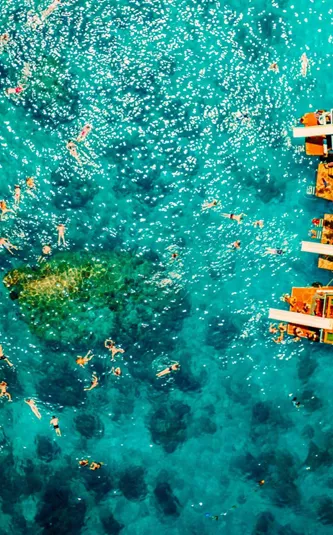 Contiki travellers swimming and snorkelling in vivid turquoise waters around traditional wooden boats anchored off the coast of a Thai island on a Thai Island Hopping East Tour