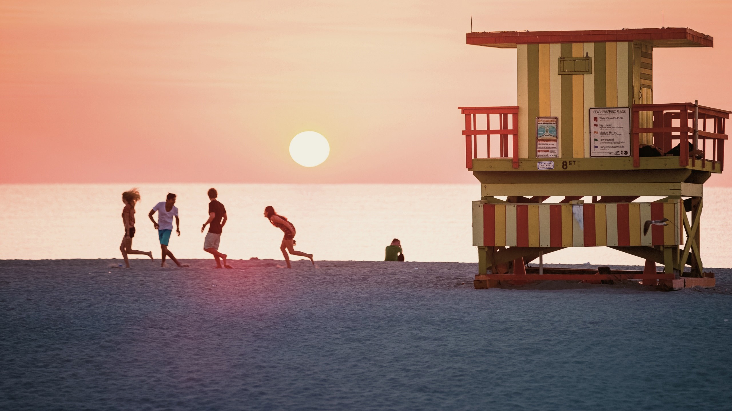 Sunset over Miami Beach with the iconic Art Deco lifeguard tower and travellers enjoying the shoreline on the Contiki Dallas to Miami Tour