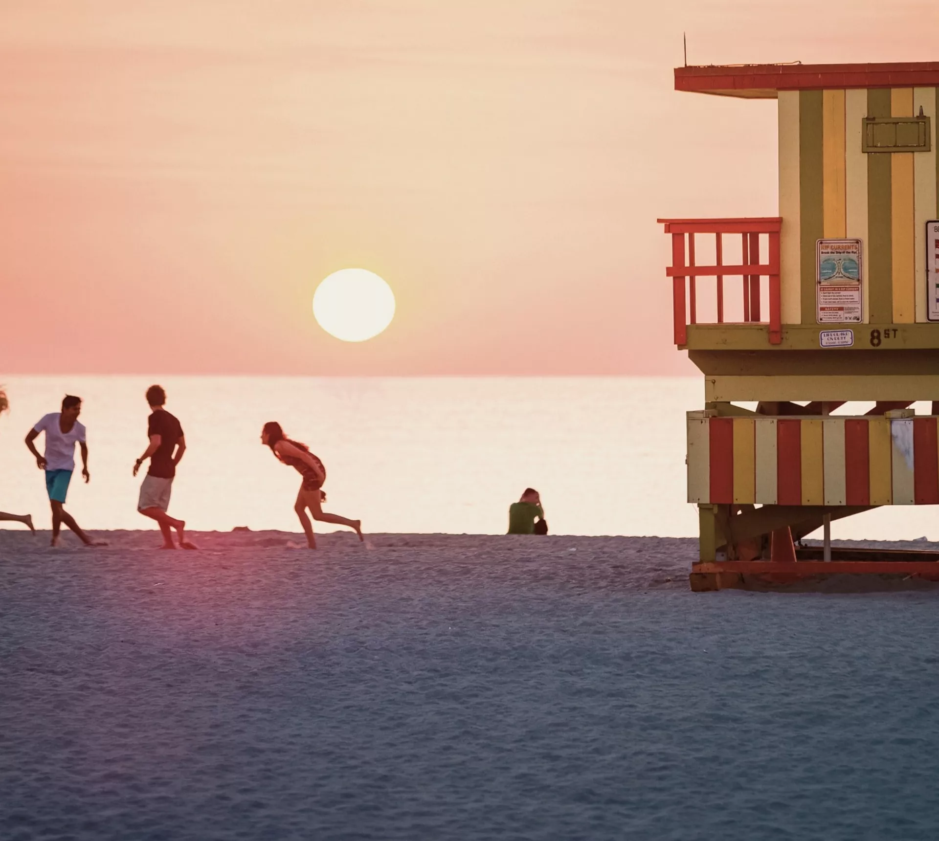 Sunset over Miami Beach with the iconic Art Deco lifeguard tower and travellers enjoying the shoreline on the Contiki Dallas to Miami Tour