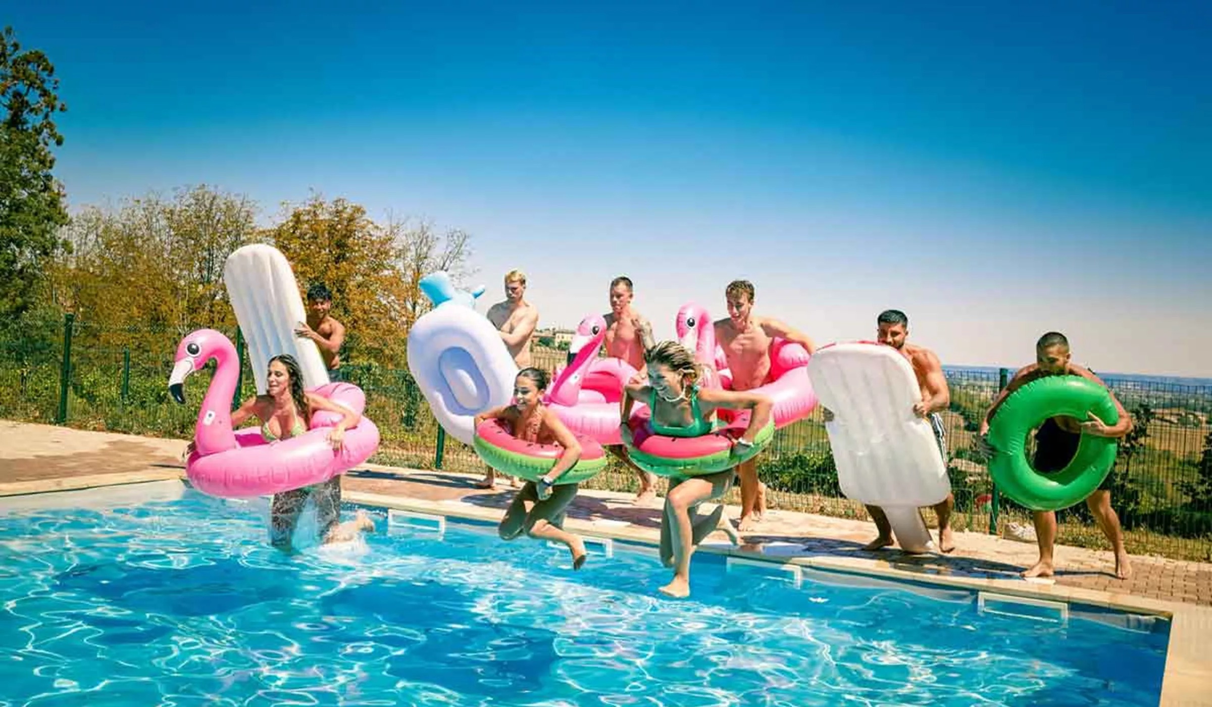 Group of young travelers jumping in pool with swim rings in France 