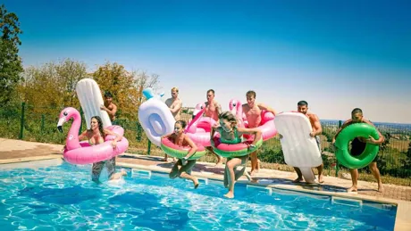 Group of young travelers jumping in pool with swim rings in France